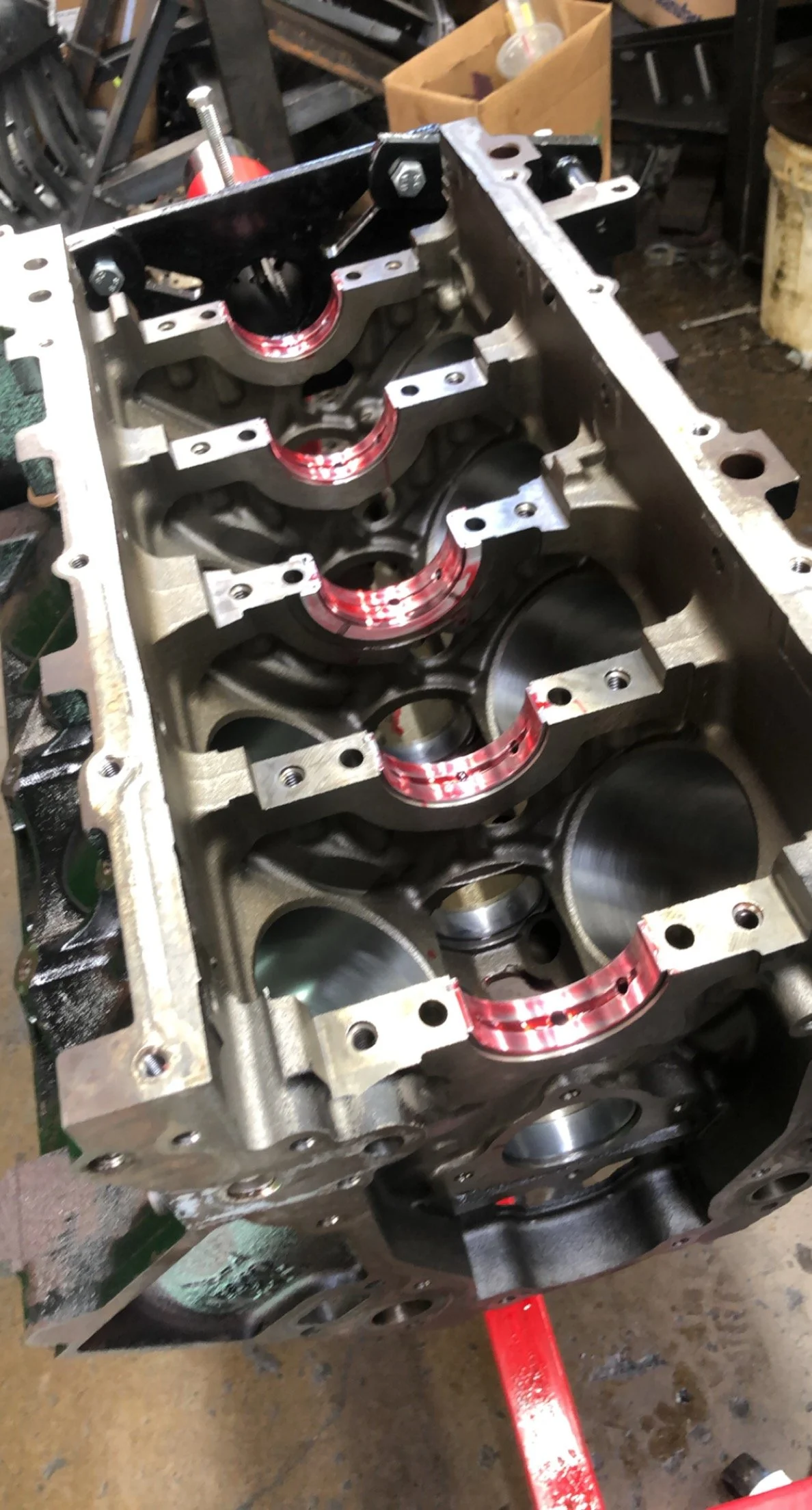 A partially assembled car engine block with visible cylinder openings, some red sealing rings, and metallic components inside a workshop.