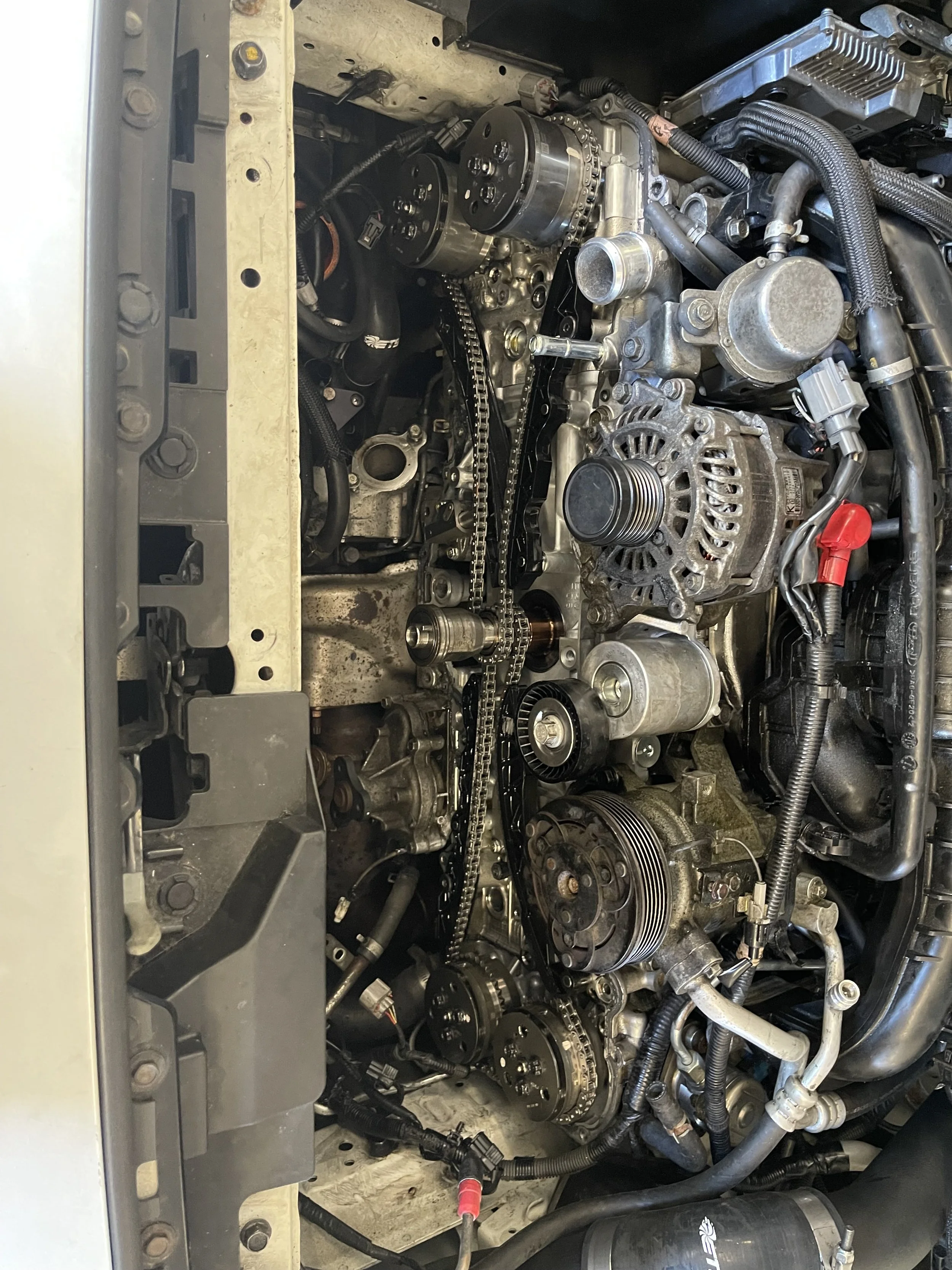 Close-up of a car engine with exposed timing chains, pulleys, and various engine components.