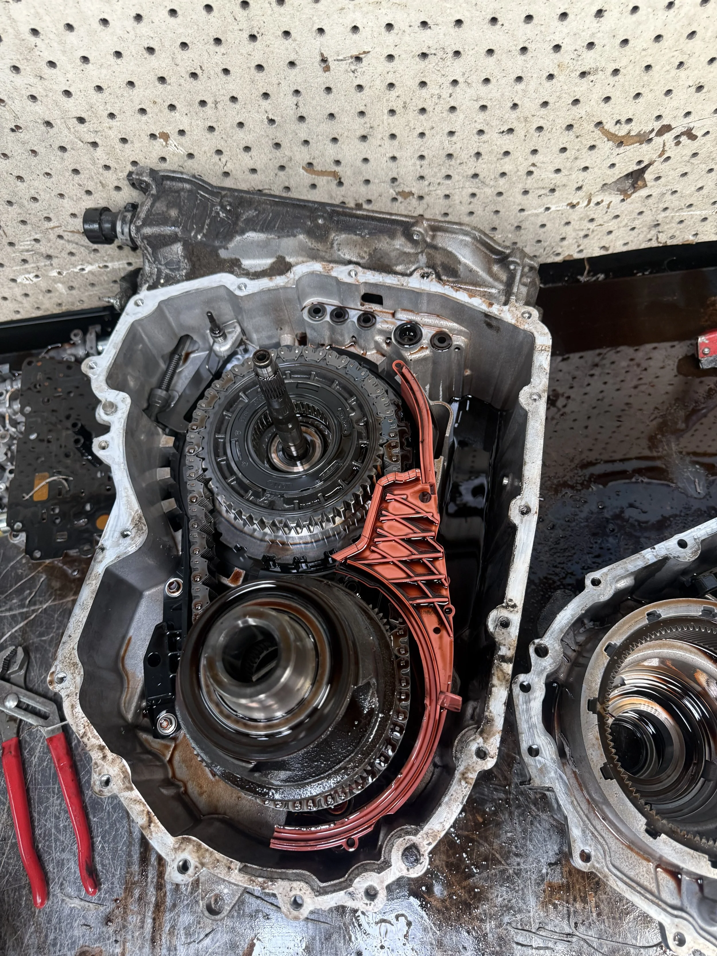 Disassembled car transmission with gears, red plastic part, and tools on workbench.