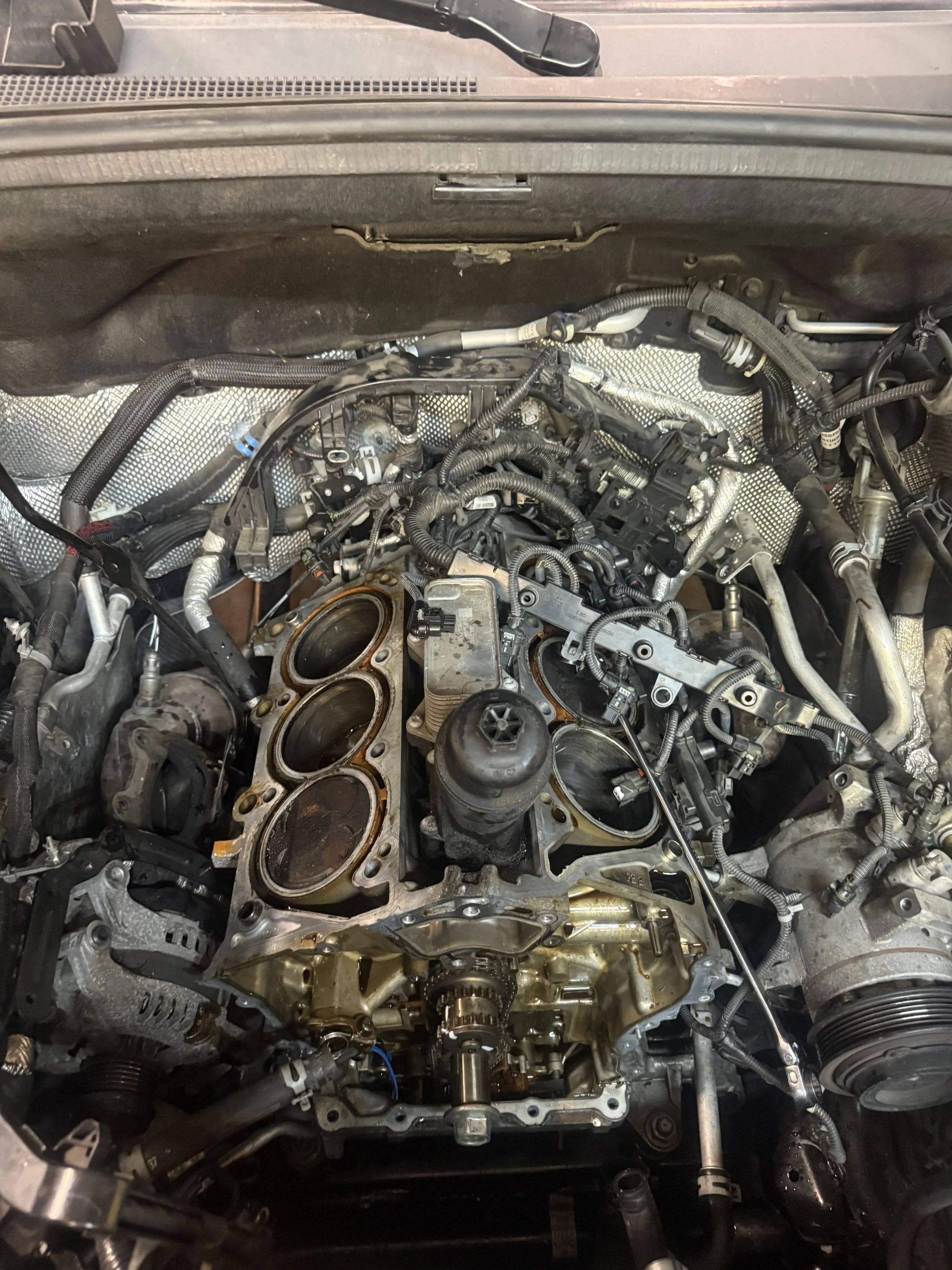 Open car engine with visible cylinders and various mechanical parts and wiring.