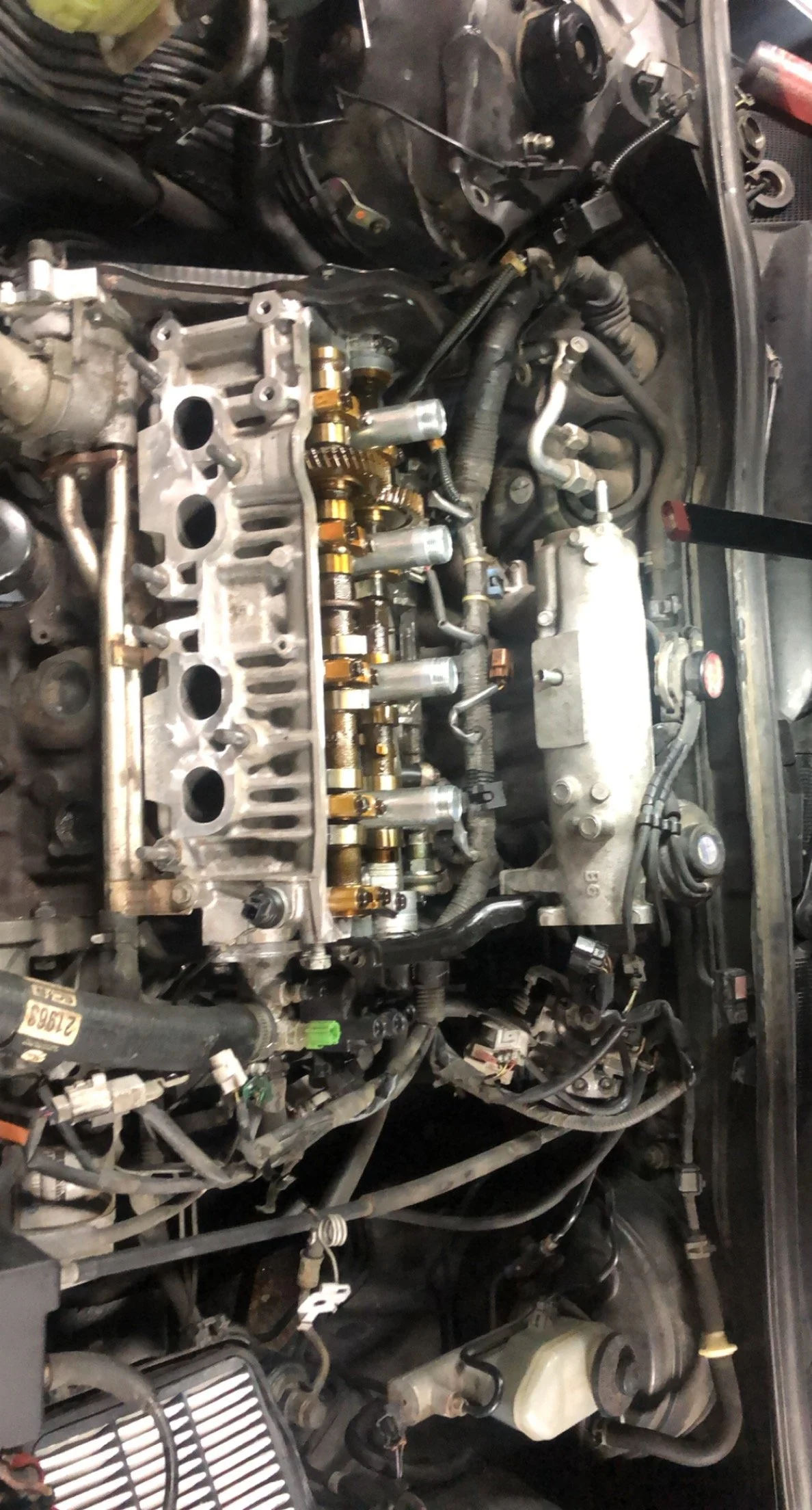 Inside a car engine bay showing the valve cover removed, exposing the camshaft and engine components during maintenance or repair.