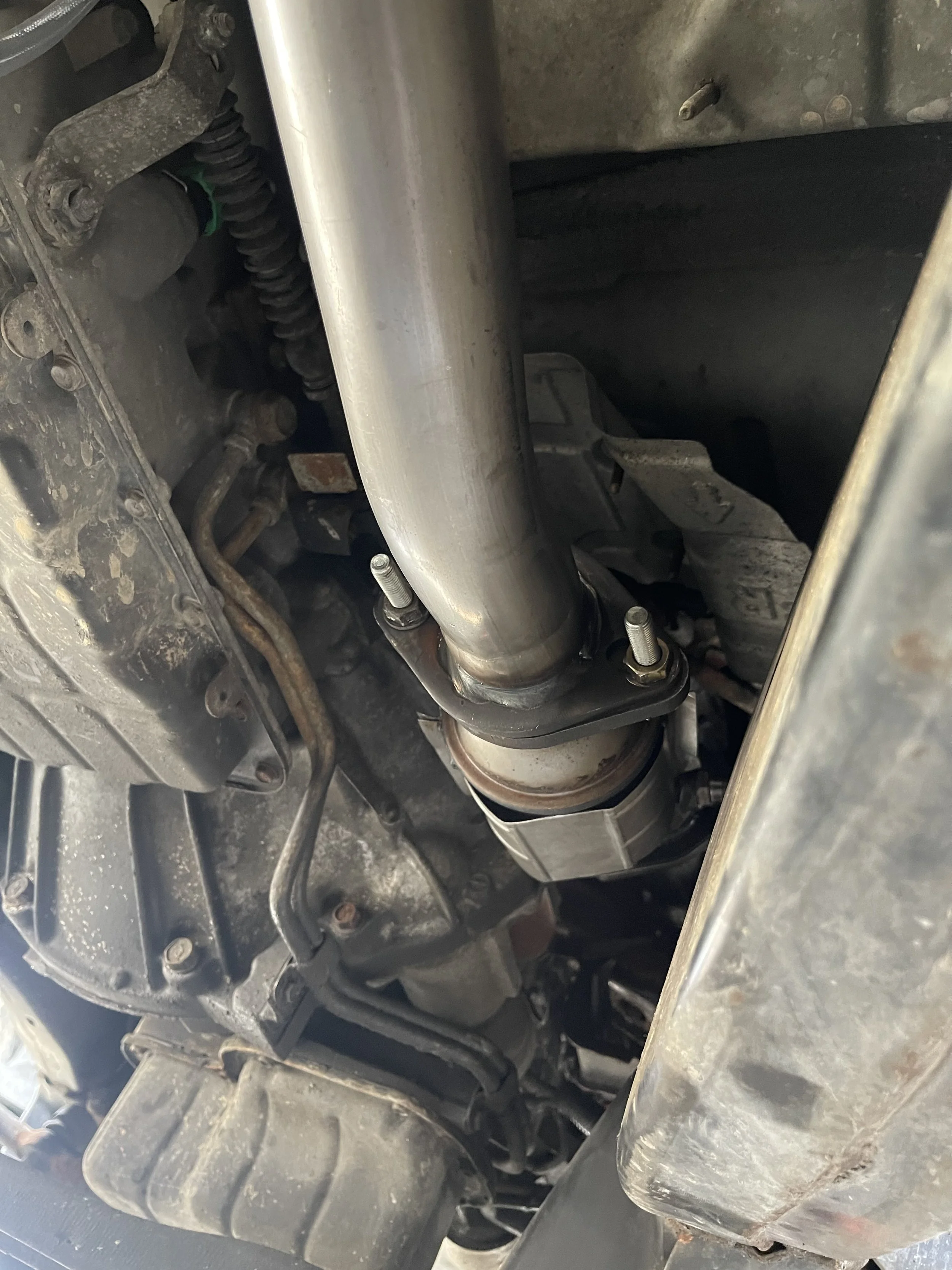Underneath a vehicle showing a large metal exhaust pipe connected to the exhaust system.