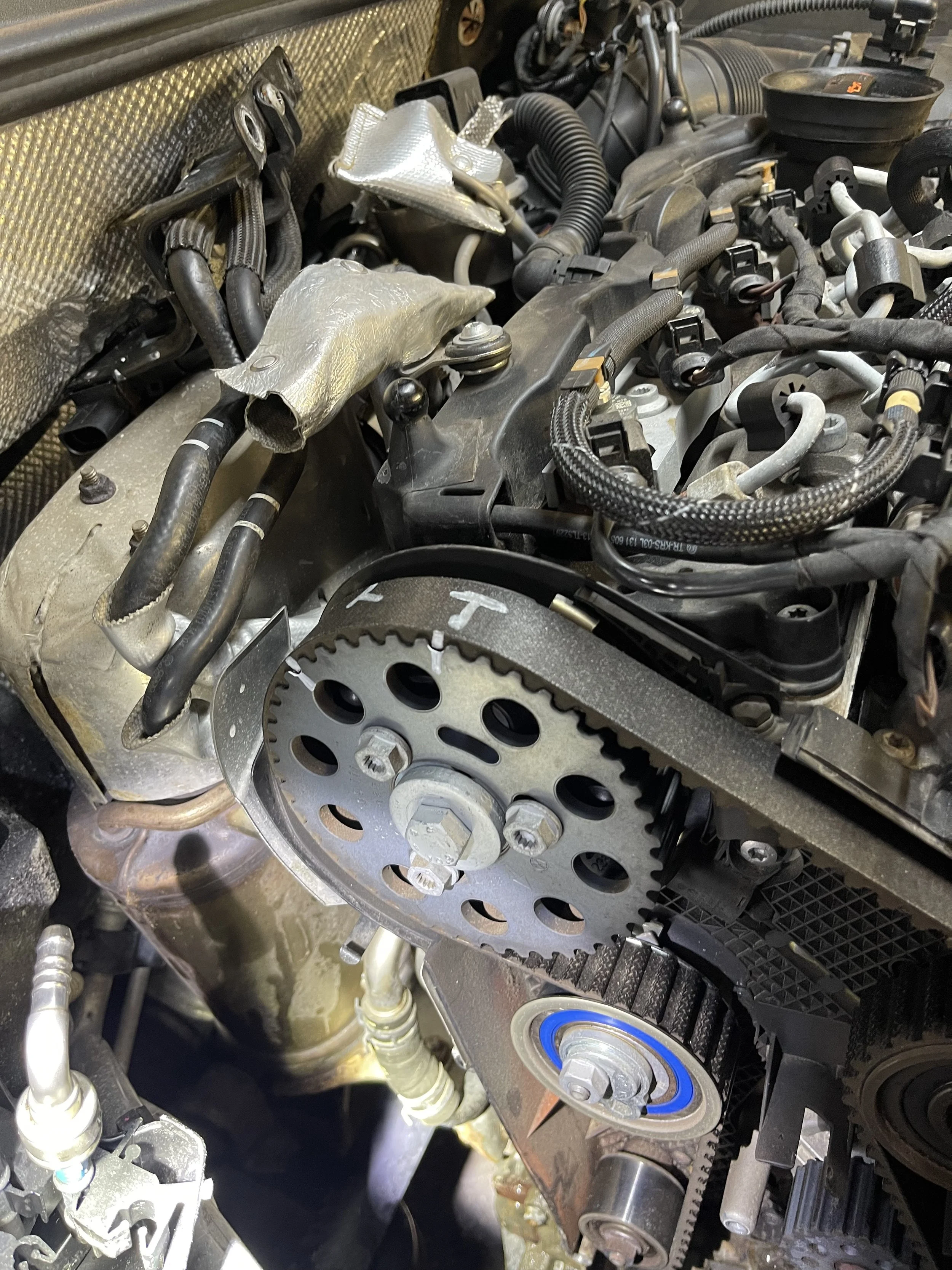 Close-up of a car engine showing timing gear and various hoses and components.