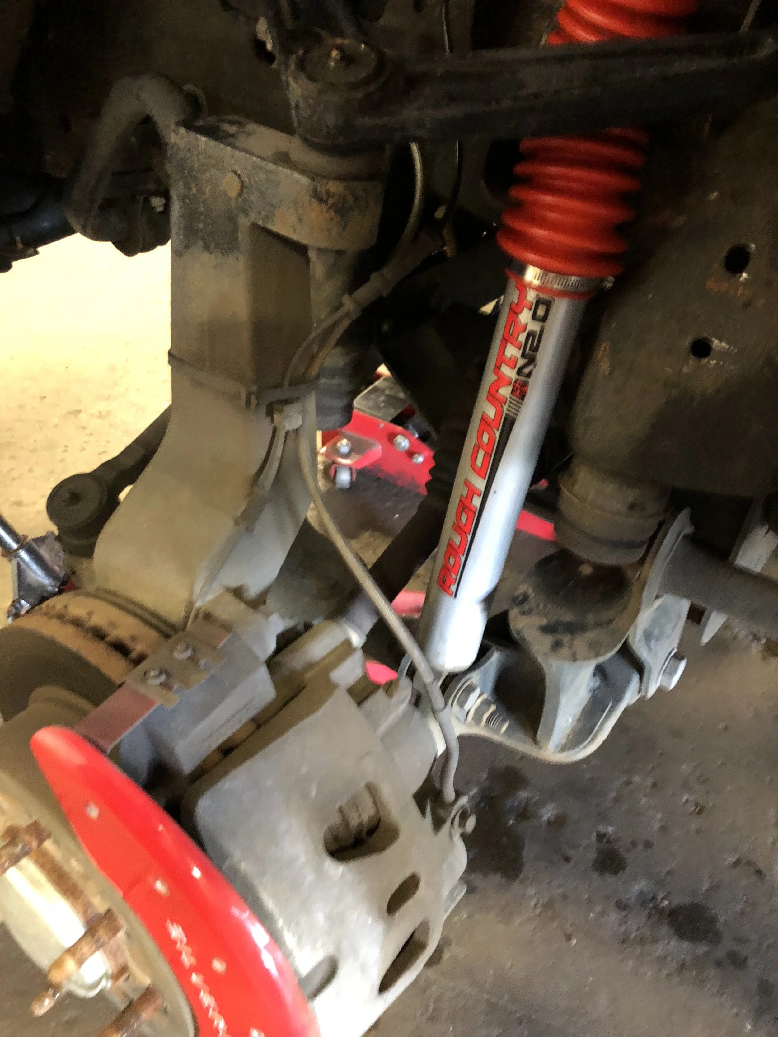 Close-up of a vehicle's suspension system, showing a shock absorber labeled 'Rough Country 2.0' and rusty components.