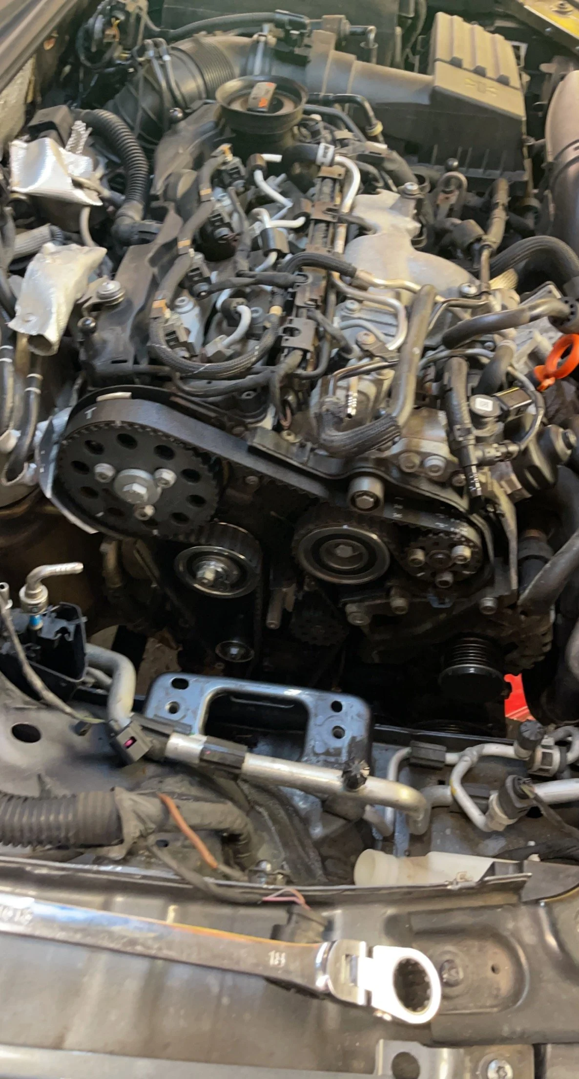 Engine of a vehicle with visible timing belt, pulleys, and various components, showing part of the engine bay.