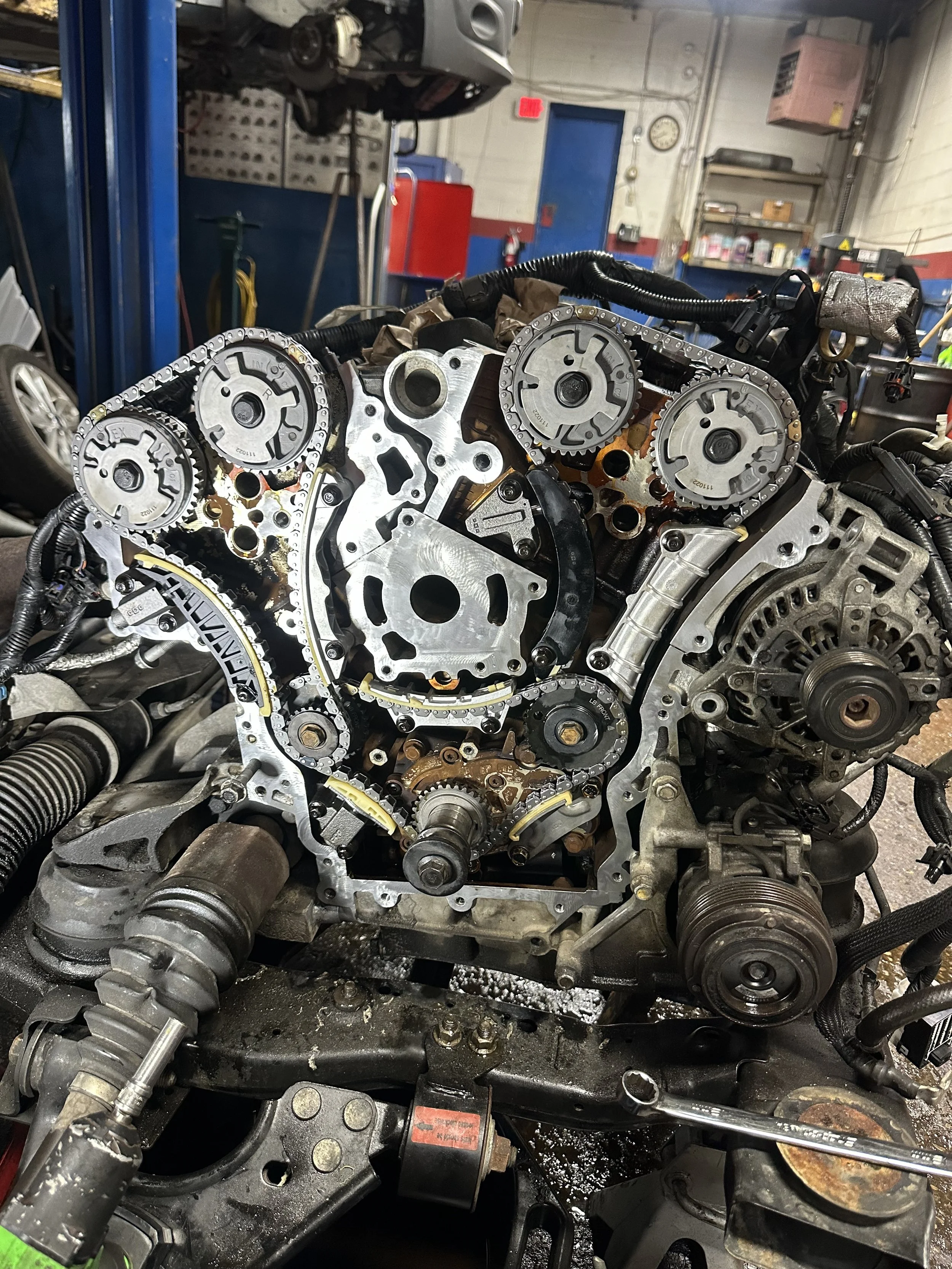 Disassembled car engine with timing chains, gears and components on a workbench in an auto repair shop.