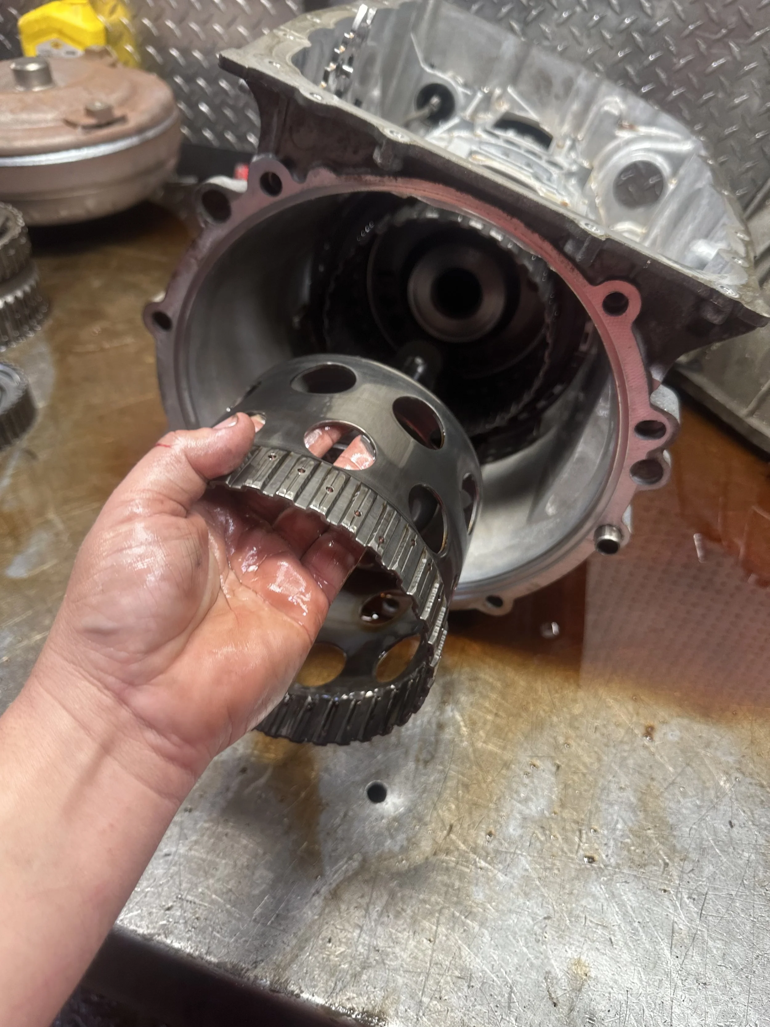 A person holding a metal ring gear inside a vehicle transmission case, with other transmission components on a workbench surrounding it.