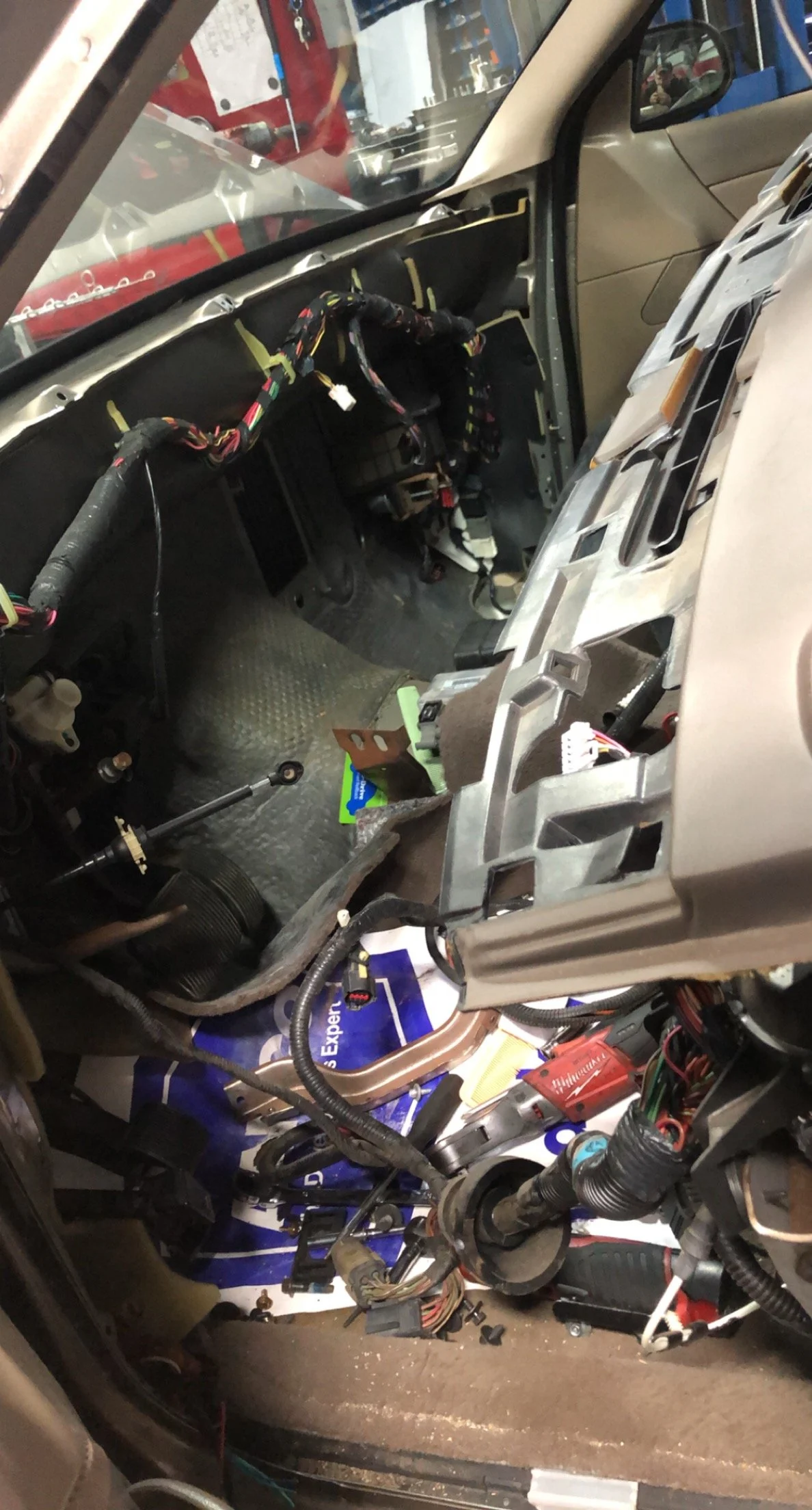 The image shows the interior of a vehicle with the dashboard removed, exposing wiring and components. Tools and parts are scattered inside the vehicle, indicating repair or maintenance work.
