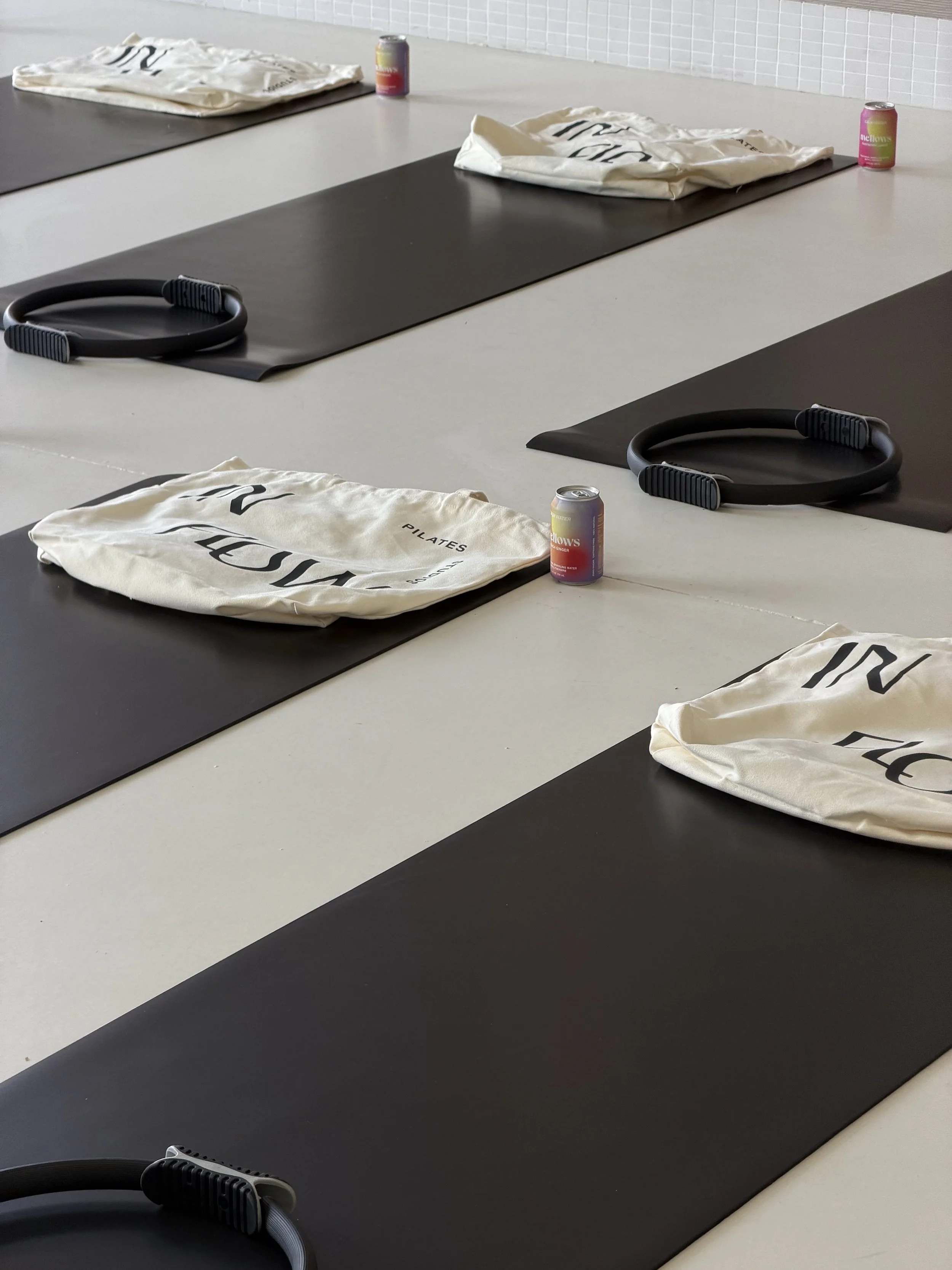 Yoga mats with black surface on a white floor, accompanied by folded white cloth bags, black resistance bands, and cans of flavored sparkling water in the Luma Space Sunshine Coast Buderim.