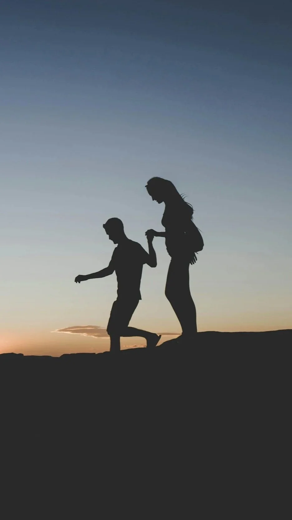 Silhouette of a woman and a boy holding hands at sunset or sunrise on a hill.