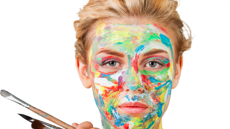 Person with colorful paint on their face holding paintbrushes.