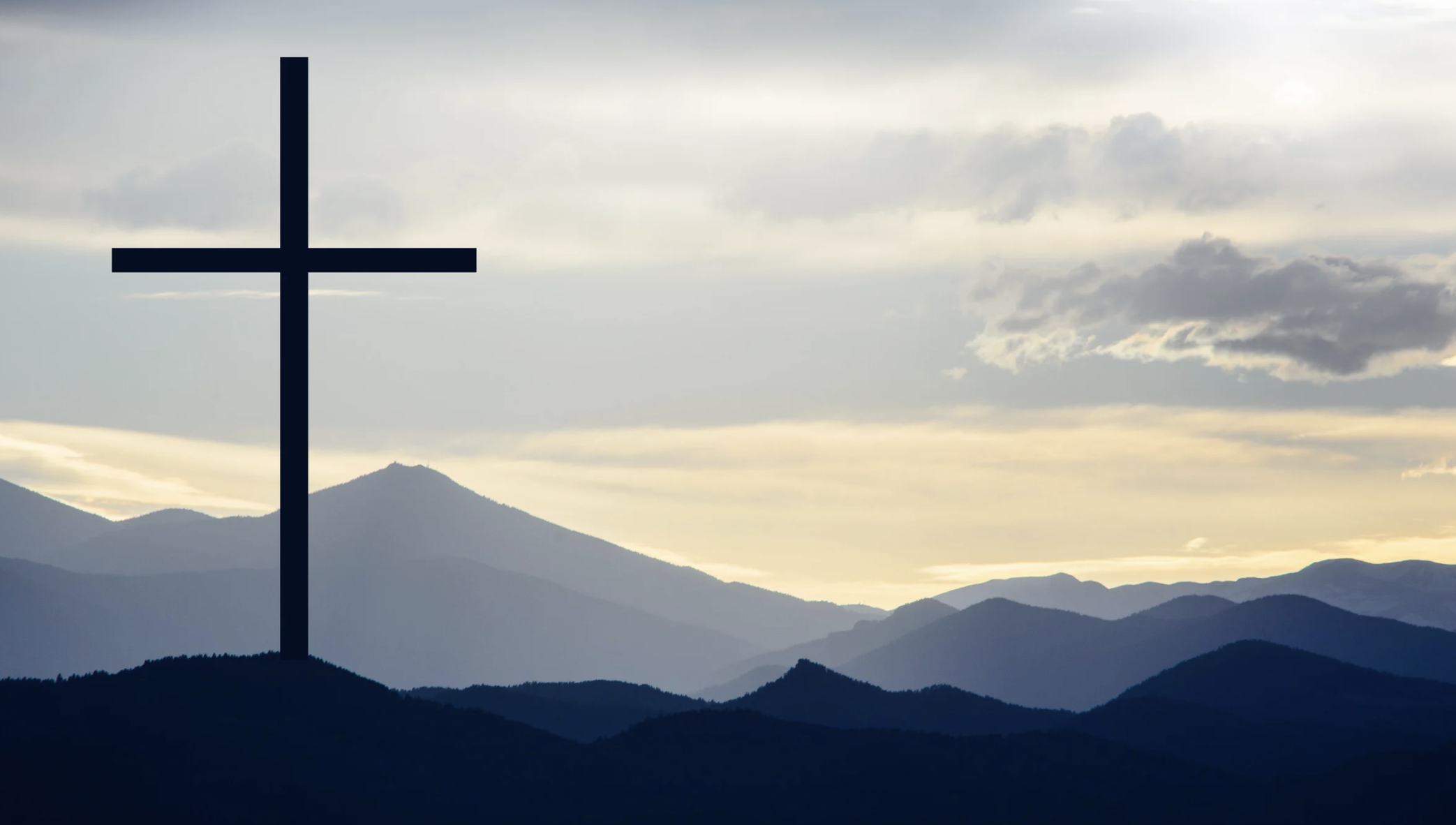 Silhouette of a cross on a mountain with layered mountain ranges and cloudy sky in the background