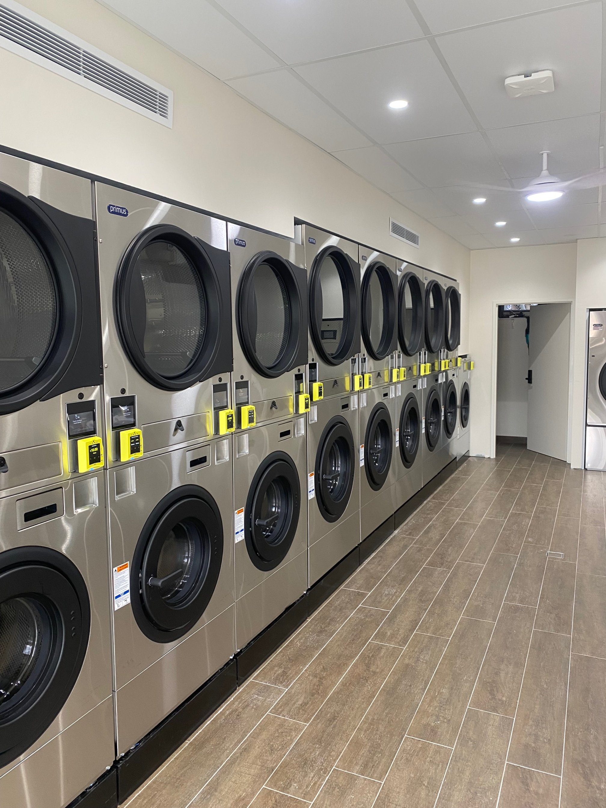 Row of stainless steel commercial washers in a laundry room.