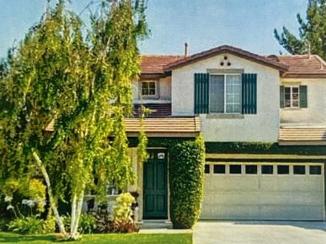 Front view of a two-story house with a garage, a large tree, and green bushes.