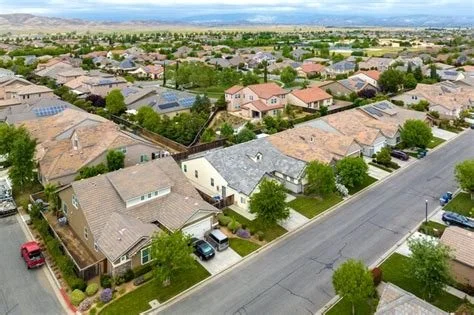 A neighborhood with single-family homes, trees, and a street with parked cars under a cloudy sky.