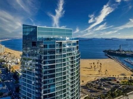 Skyline of a modern high-rise building by the ocean with a sandy beach and docks in the background.