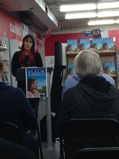 Fleur stands at the front of a bookstore at an event, talking to readers