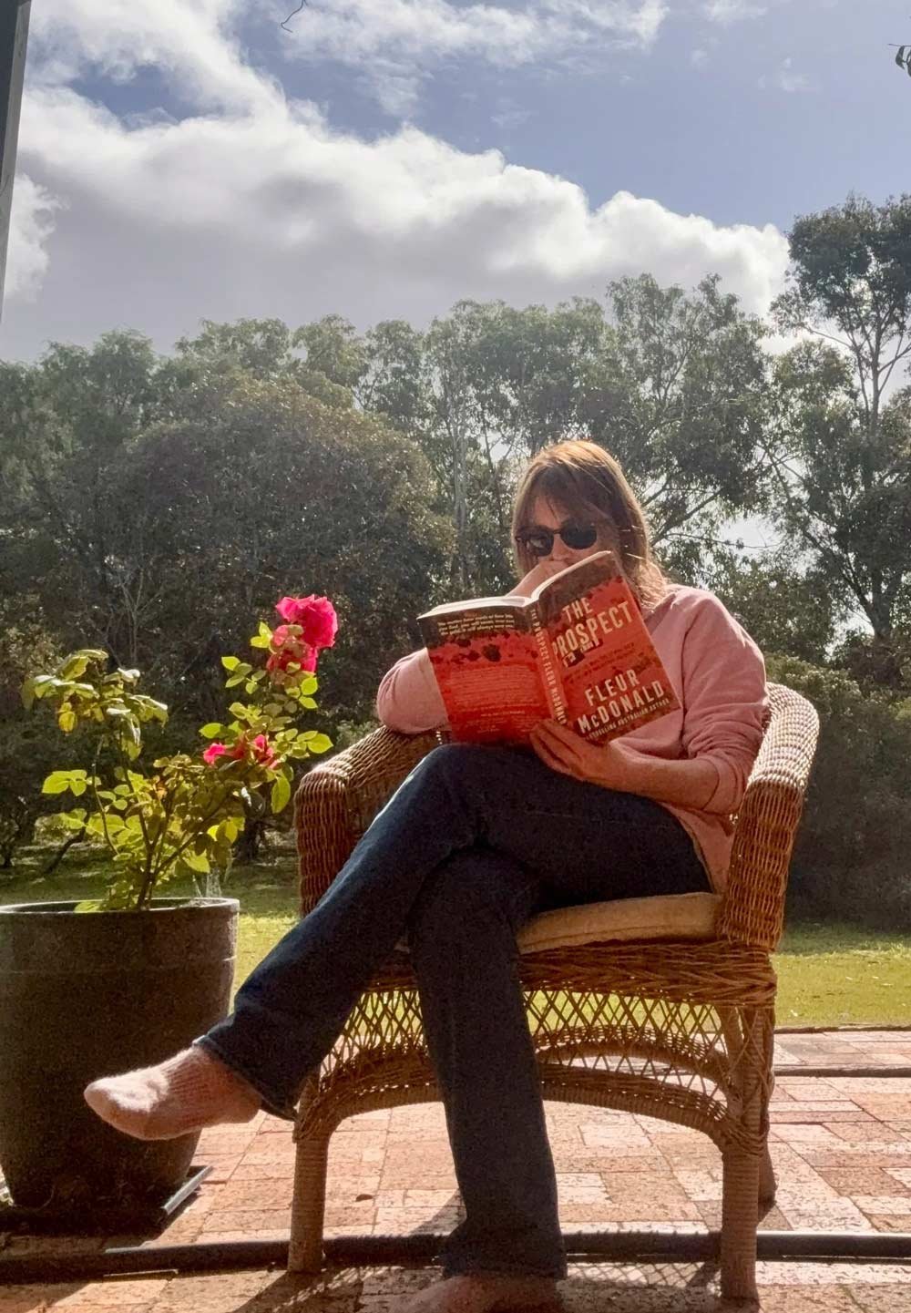 Fleur sits out on a patio on a wicker chair reading a copy of The Prospect