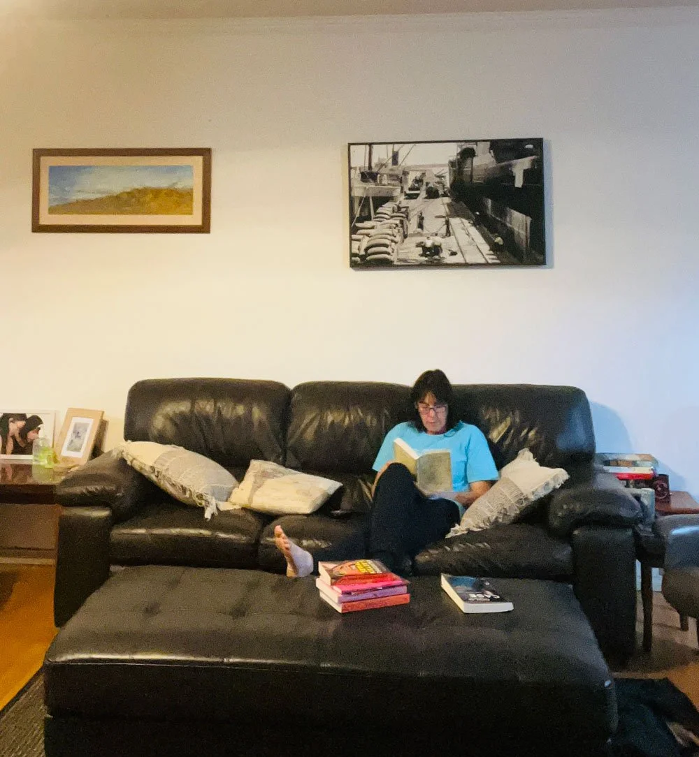Fleur sits on the lounge with a book in her hands reading. There are a stack of books in front of her.