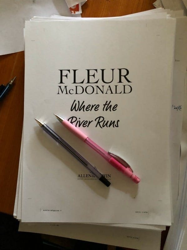 Printed manuscript pages for Where the River Runs. Two pens sit on top. One black, one red.