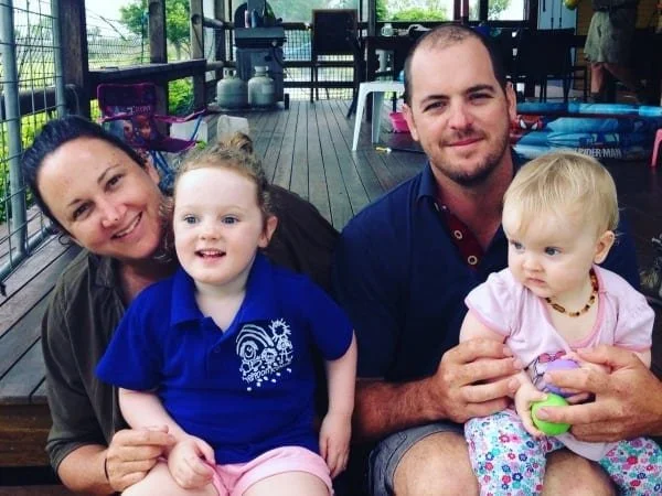 A happy family. A woman and man sit smiling, each has a small child on their lap.