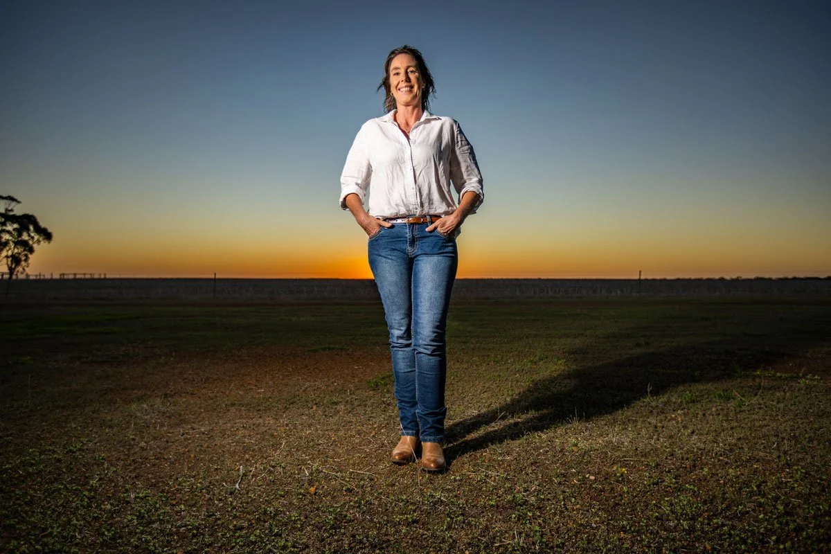 Books by Fleur McDonald - Fleur stands smiling with her hands in the pockets of her jeans. She' on the land, behind her the sun is setting.