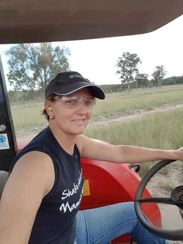 A woman driving a tractor smiles at the camera