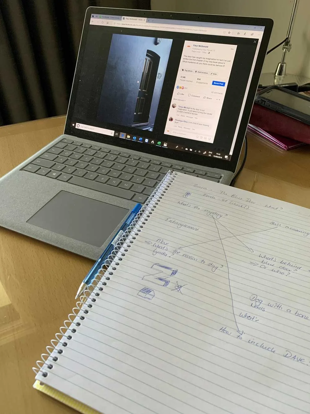 A picture of a blue door on a laptop on a desk. Next to it is a notebook with lines crossing over to different ideas