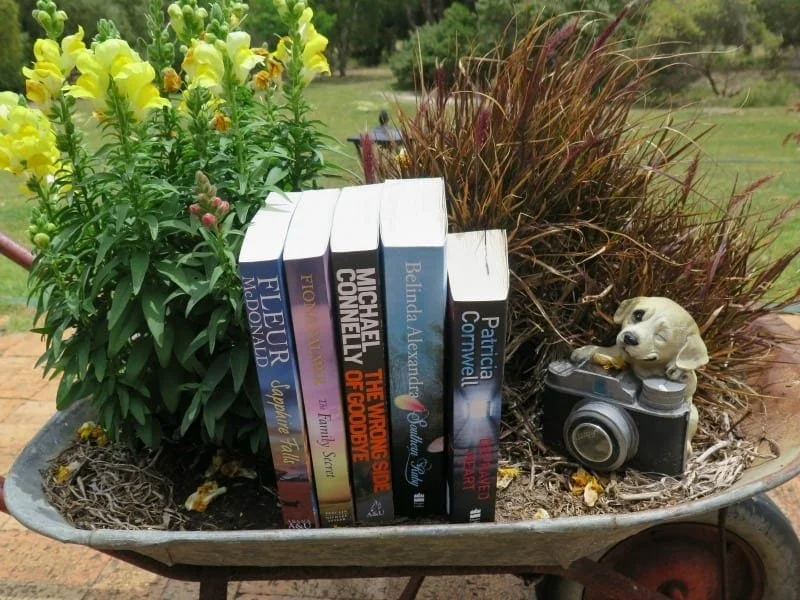 Five books sitting nicely in a wheelbarrow with flowers