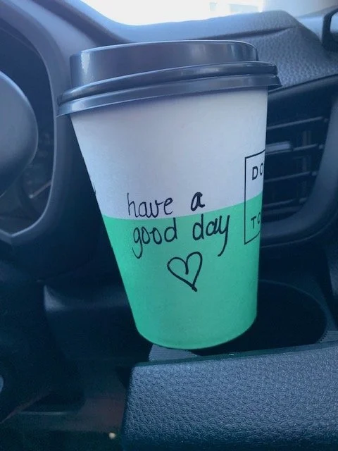 Coffee cup in a car - written on the outside of the cup in black texta is 'Have a good day' with a love heart