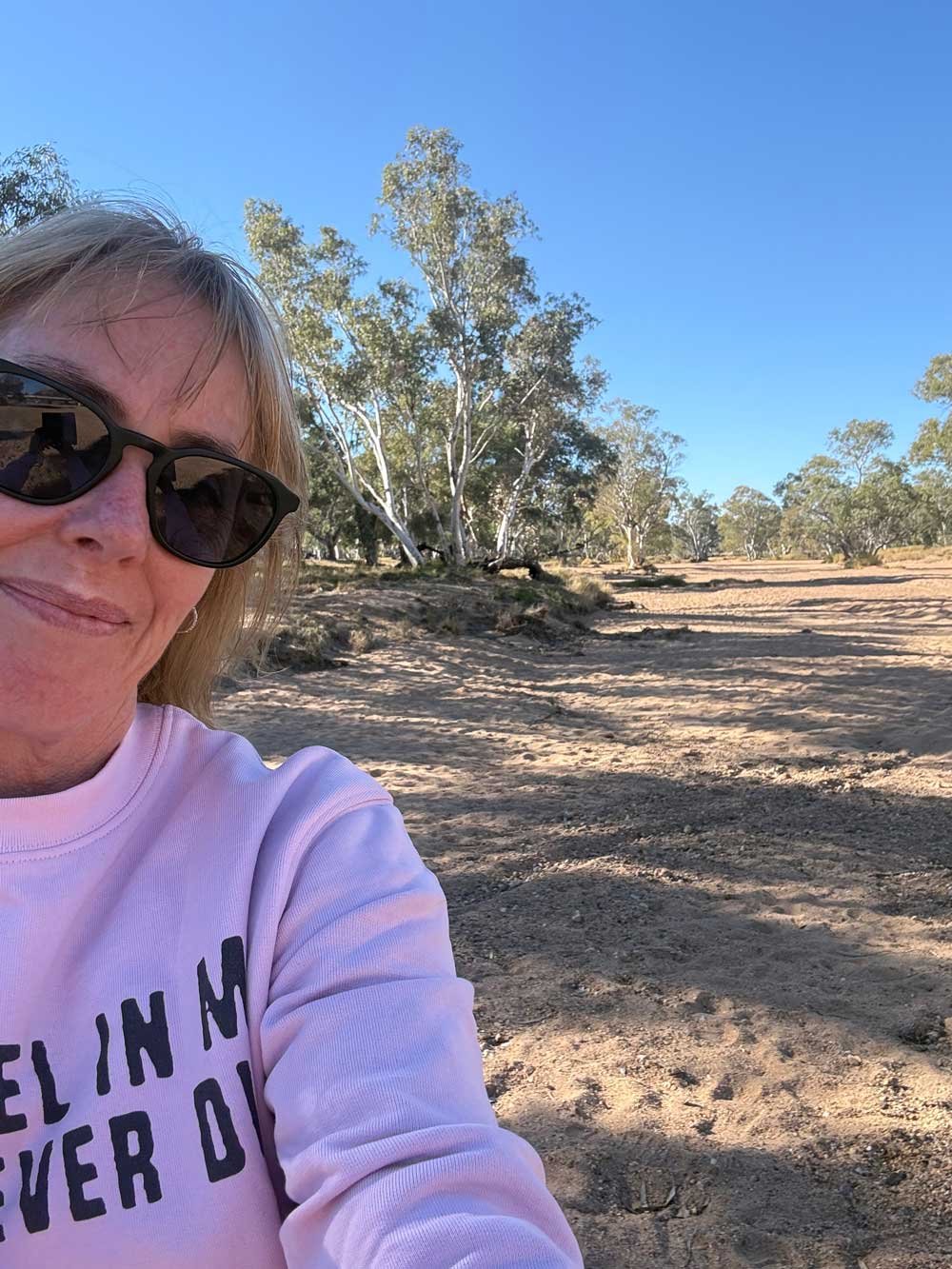 Fleur stands smiling showing The Alice. A blue sky, trees bending and a dirt road