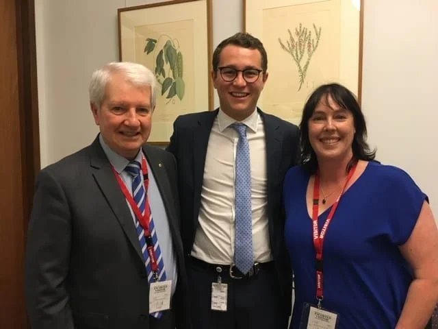 Fleur stands next to two men in suits, all are smiling.