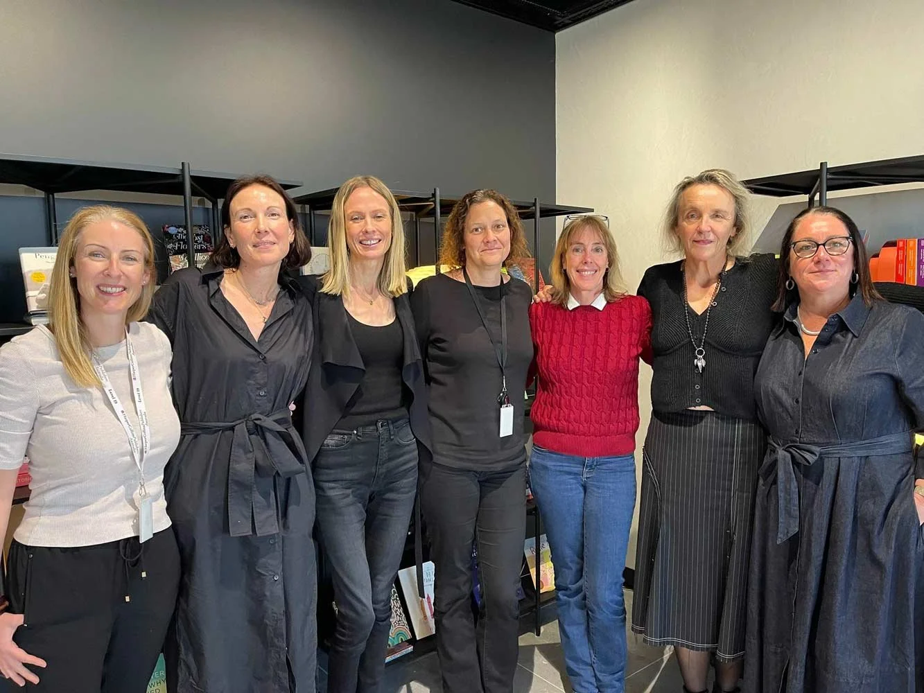 7 Women standing shoulder to shoulder with their arms around each other with big smiles on their faces