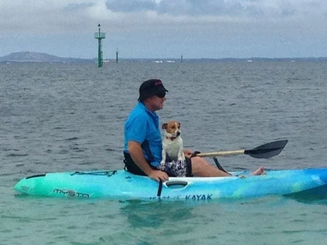 A man on a kayak on the water with a jack russell on his lap