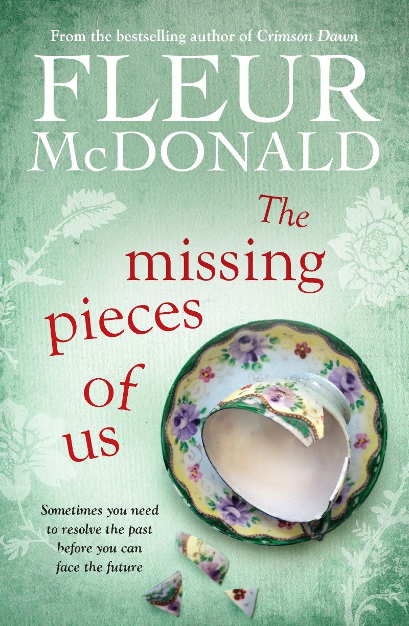 The Missing Pieces of Us book cover by Fleur McDonald. Green textured background with flowers. A broken tea cup on a saucer with pieces next to it