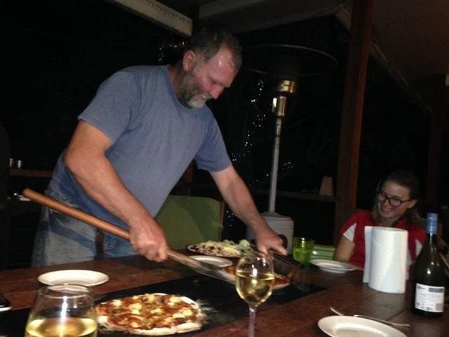 A smiling man dishing out fresh pizza from a pizza oven