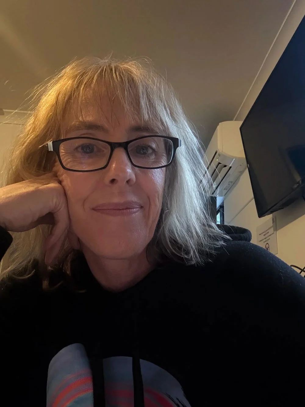 A photo of Fleur smiling with her head resting on her hand as she looks directly at the camera.