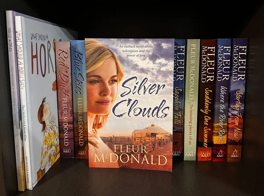 The book, Silver Clouds, sits face out on a bookshelf. Behind it are all Fleur's other novels and 2 children's books.