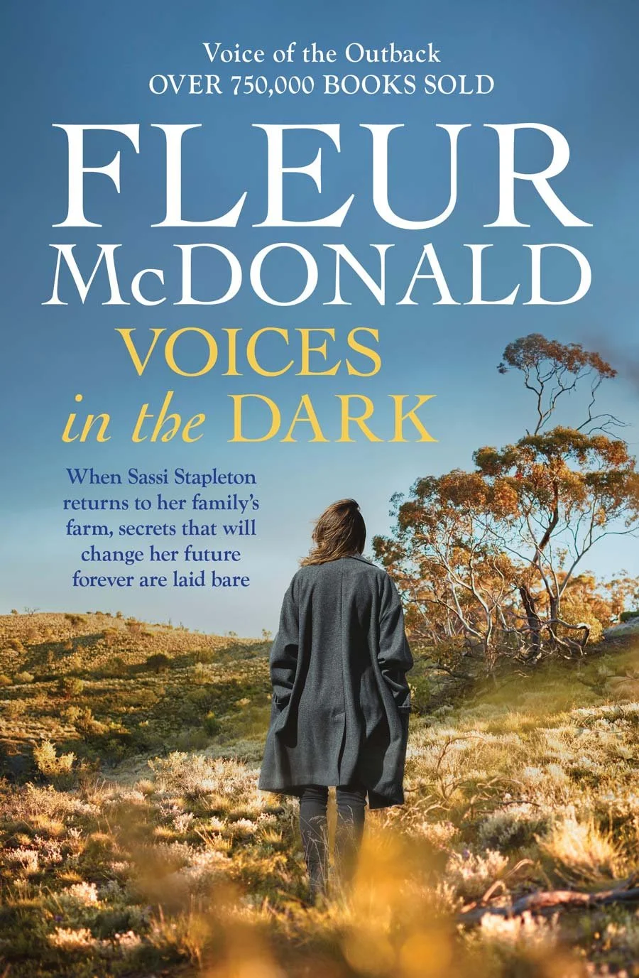 Book cover for 'Voices in the Dark' by Fleur McDonald featuring a woman walking away in a rural landscape with trees and grass under a blue sky.