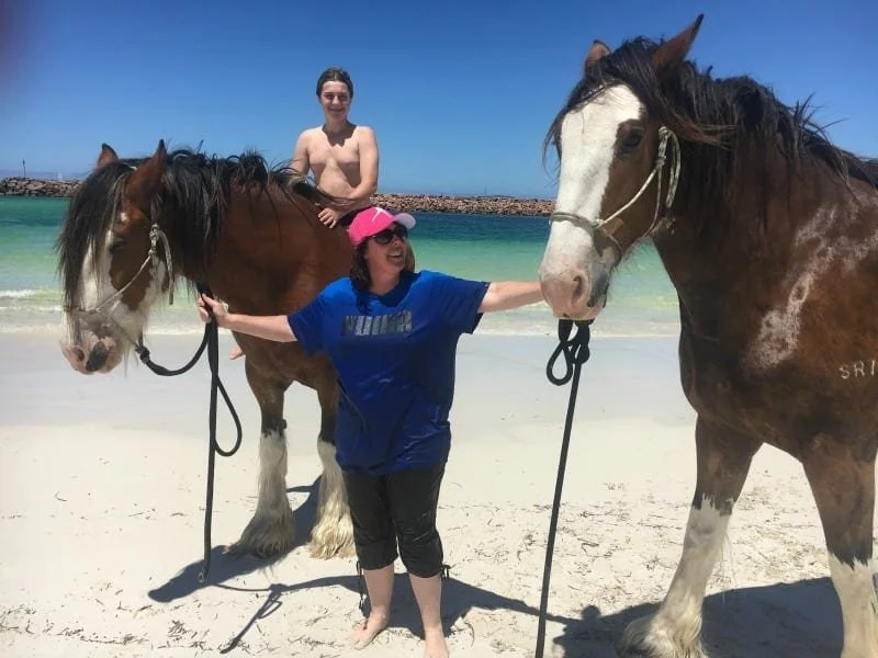 Fleur stands in the middle of two beautiful horses on the beach.