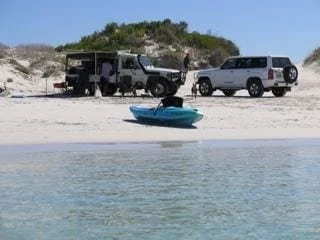Two forwheel drives up on the beach with a little lift out for cooking and a kayak on the beach