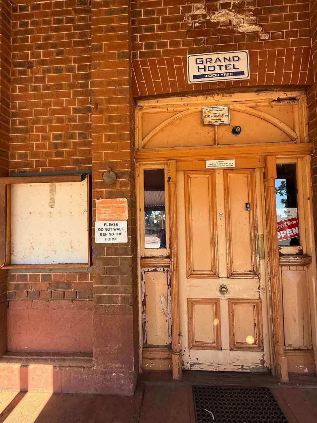 The entry door into the Kookynie Pub A wooden door with peeling paint and signs around it