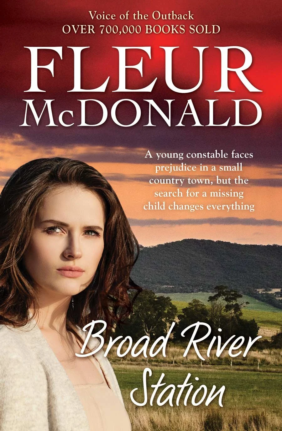 Book cover featuring a young woman with brown hair against a rural landscape with hills and trees at sunset, titled "Broad River Station" by Fleur McDonald, promoting her novel about a young constable in a small town confronting prejudice and searchi