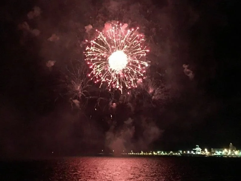 A red ball of fireworks going off over water at night