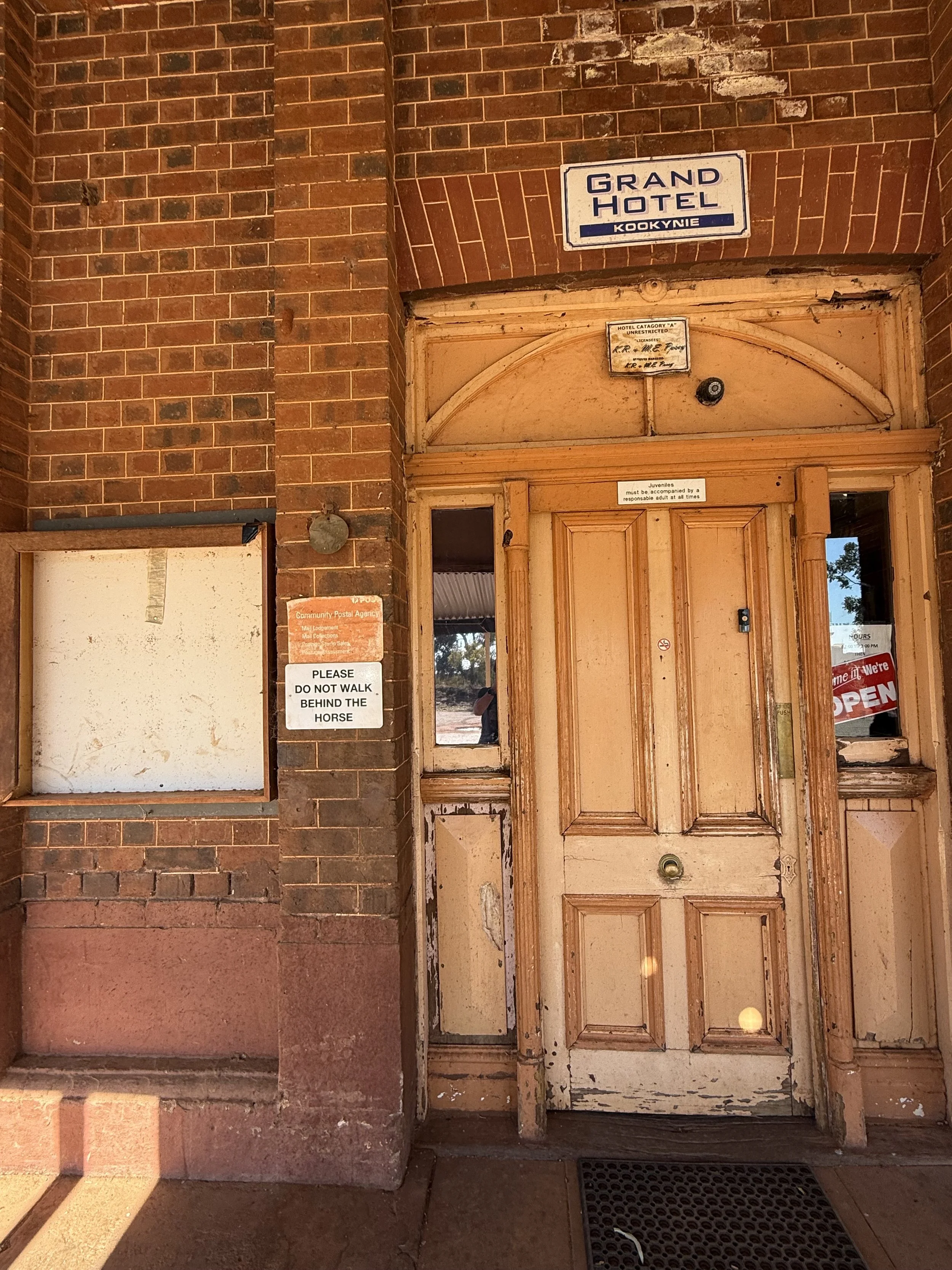 The entry door into the Kookynie Pub A wooden door with peeling paint and signs around it