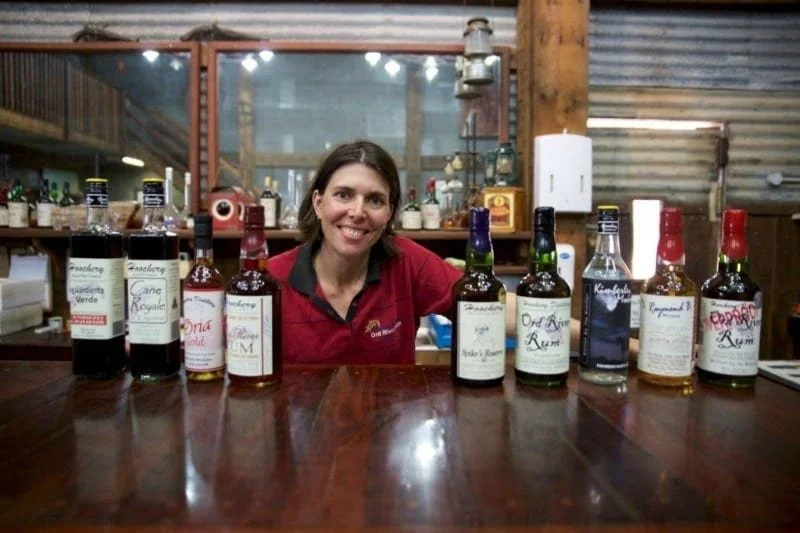 A woman leans behind a bar behind a line of alcohol.