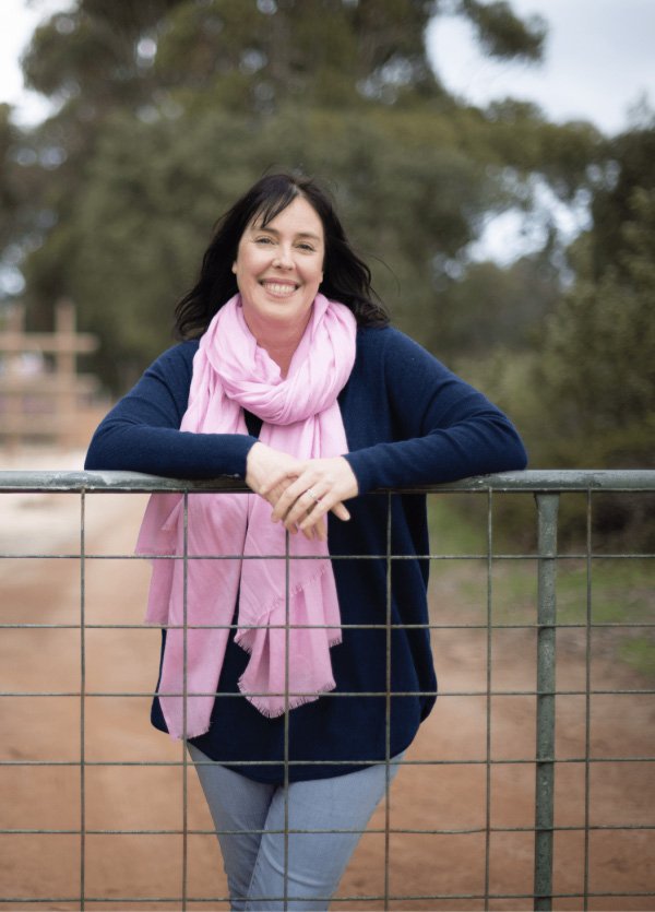 Flear stands with her arms over the gate of a fence smiling