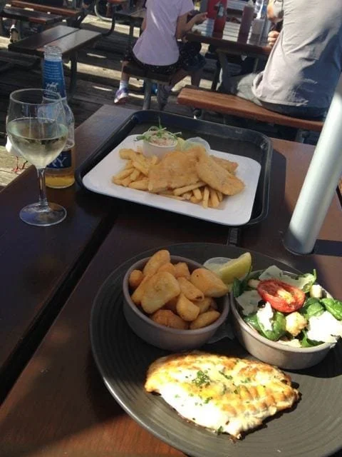Photo of two meals at an outside table - seafood, chips and salad