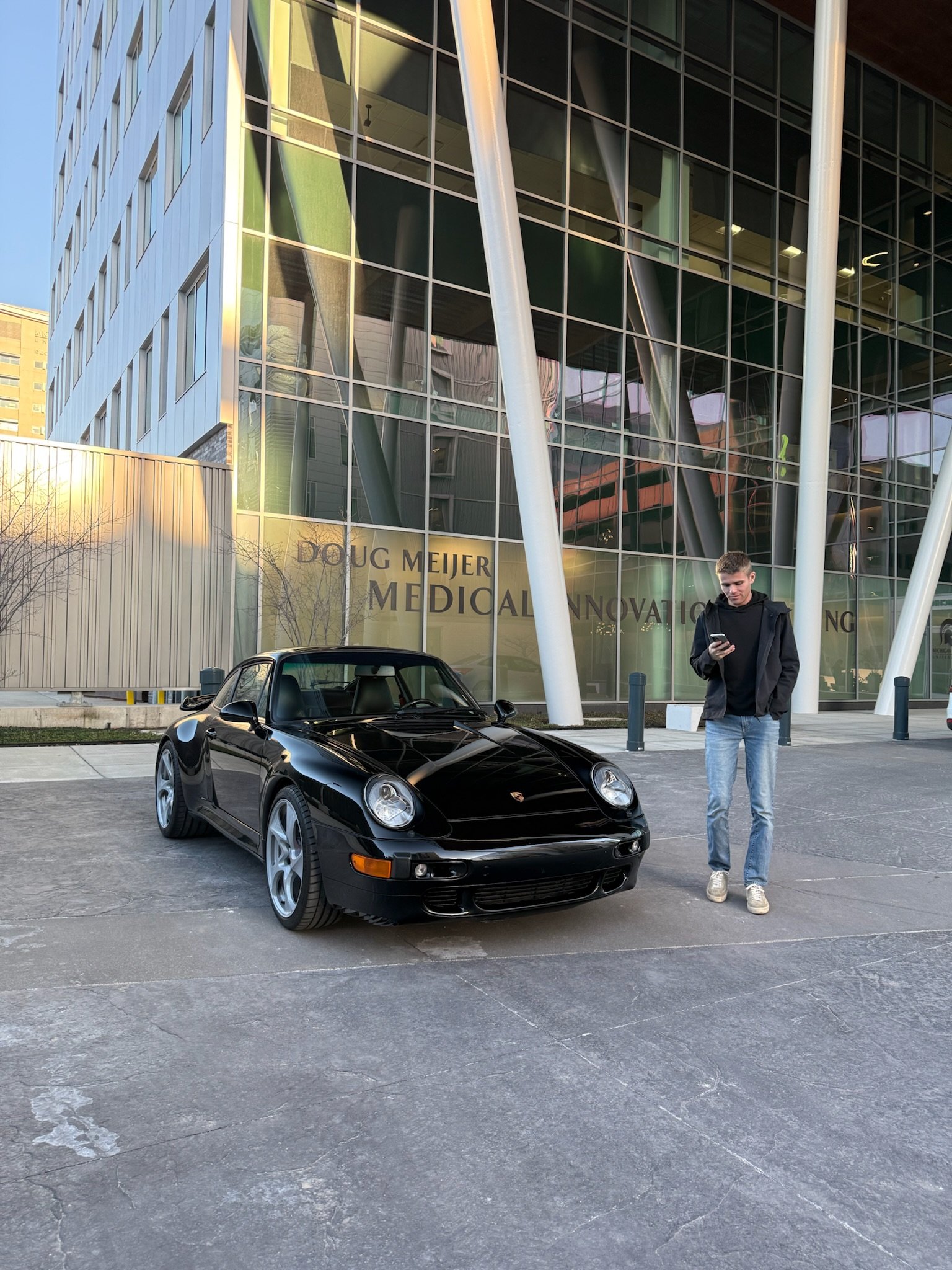 Sawyer Fleet's founder, Joseph Elkins, responding to a message on his phone, standing next to a 993 Turbo, around Medicle Mile in Downtown Grand Rapids.