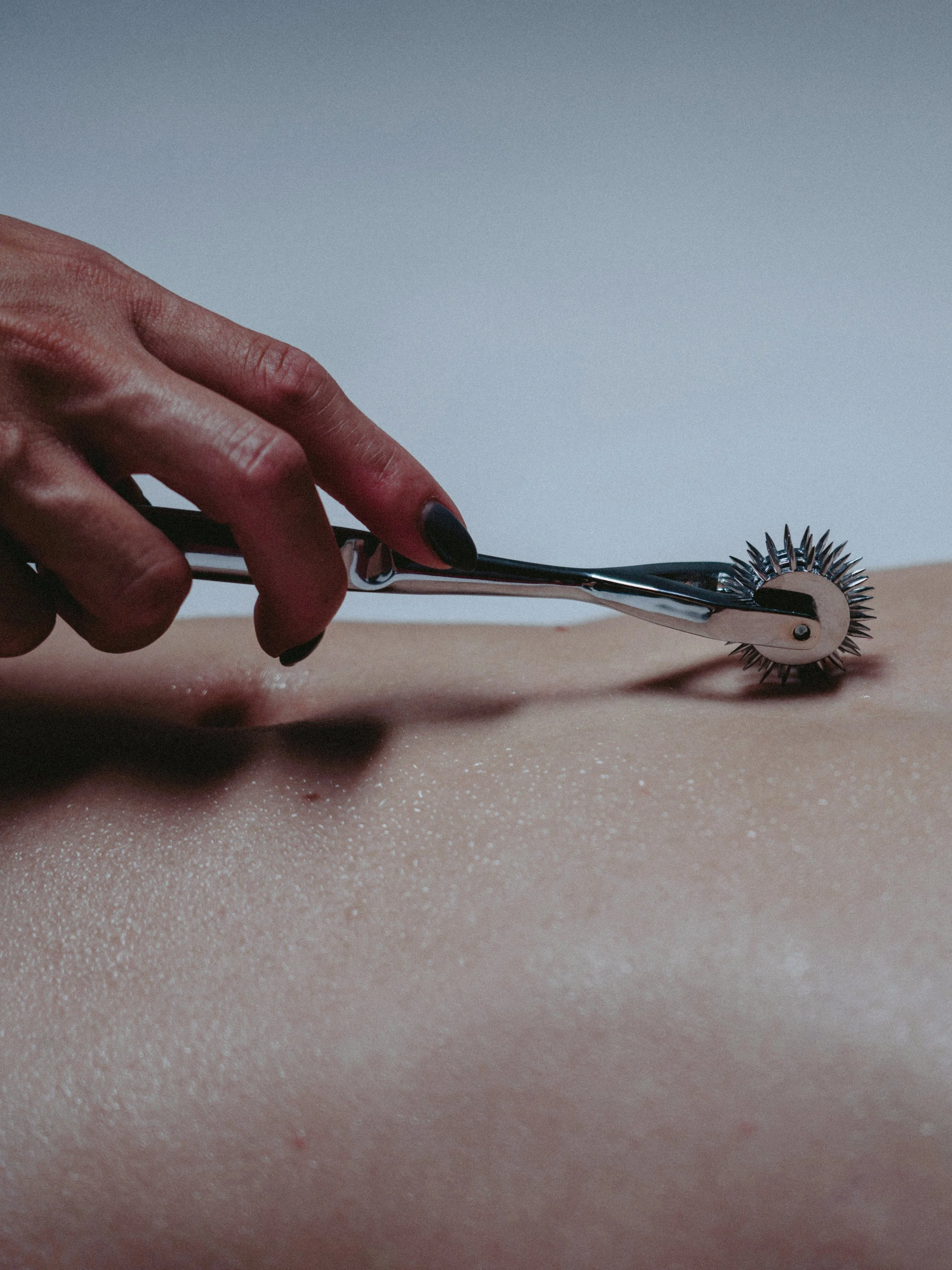 Close-up of a tattoo machine needle covered with a protective plastic cover, with a cloudy sky in the background.